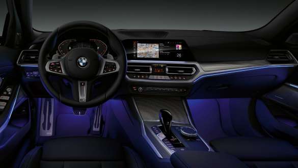BMW Série 3 Berline (G20), éclairage d’ambiance. Vue de face du poste de conduite côté conducteur de la BMW Série 3 Berline (G20) avec espace aux pieds baigné de lumière bleue diffusée par l’éclairage d’ambiance.