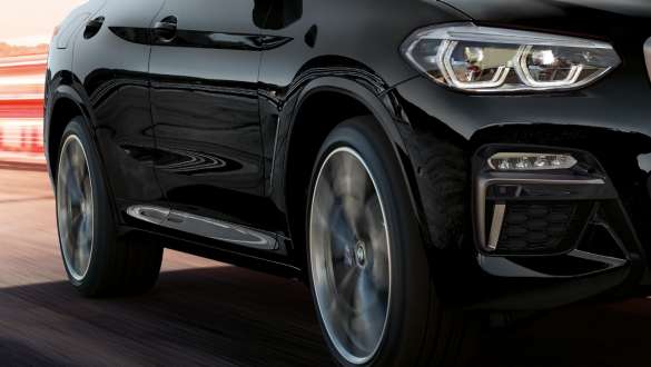 BMW X4 M40i vue de trois quarts de profil. Extérieur des BMW X4 M40i en Saphierschwarz metallic, en mouvement, vue de trois quarts de profil avec jantes BMW en alliage léger en rotation.
