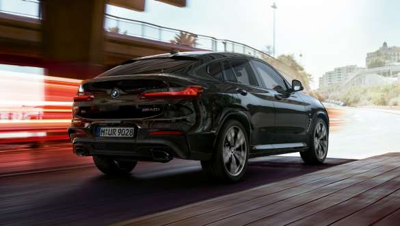 BMW X4 M40i, vue de trois quarts arrière. Extérieur de la BMW X4 M40i en Saphierschwarz metallic, en mouvement, vue de trois quarts arrière avec bandes lumineuses.