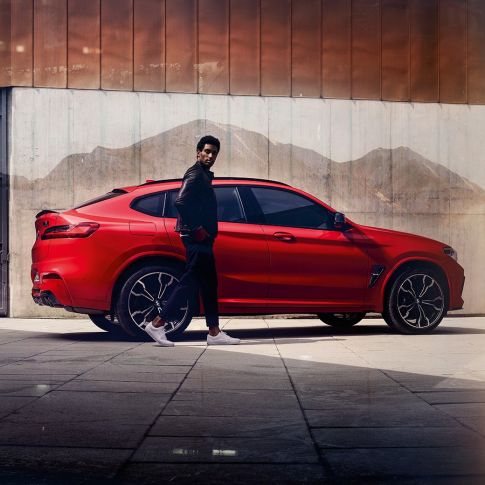 BMW X4 M Competition, vue de profil avec jeune homme. Extérieur de la BMW X4 M Competition en Toronto Rot metallic, vue de profil avec jeune homme.