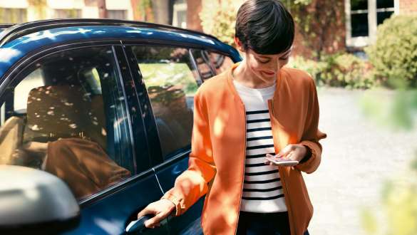 Une femme regarde son smartphone et ouvre la porte de sa BMW BMW Teleservices, une femme regarde son smartphone et ouvre la porte de sa BMW