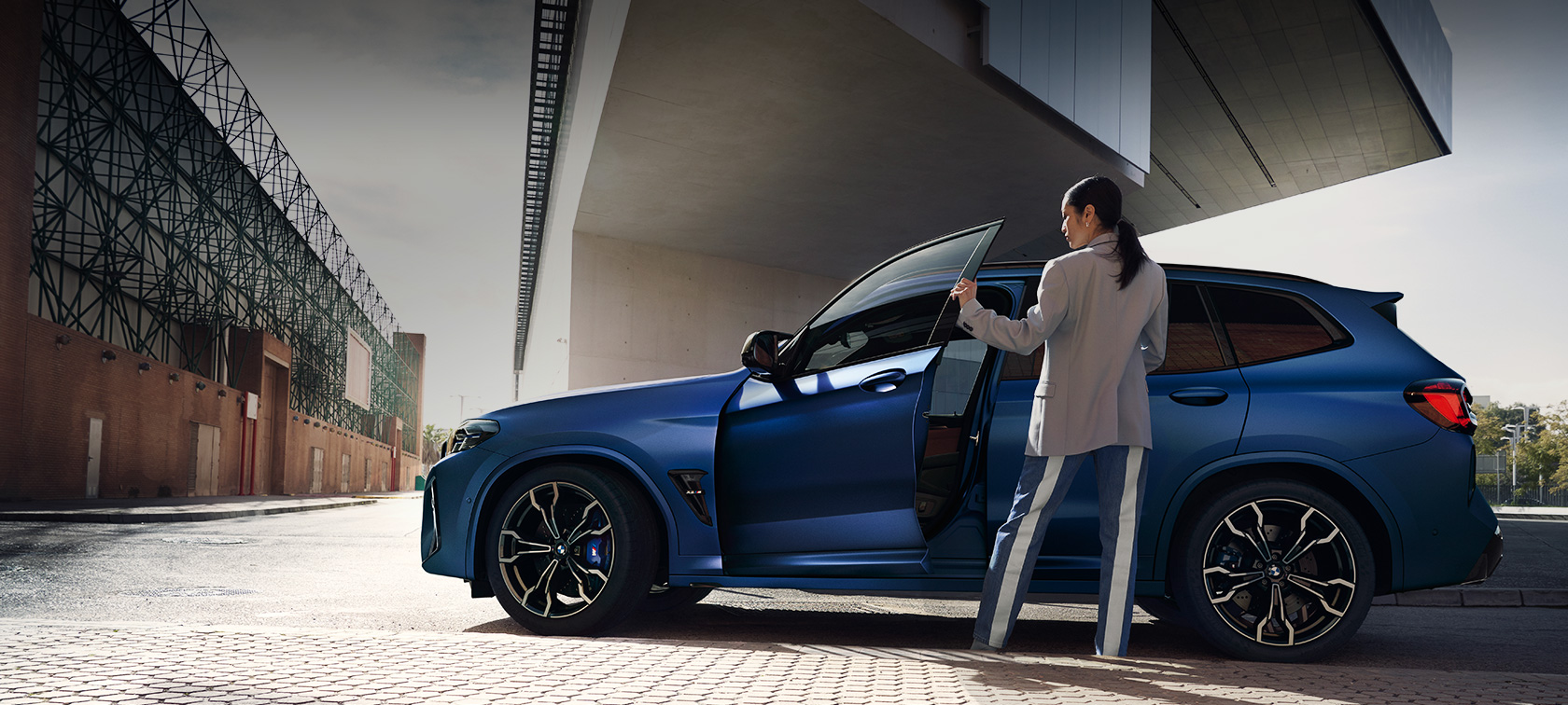 BMW X3 M Competition F97 LCI restylage 2021 vue de profil en stationnement BMW X3 M Competition F97 LCI restylage 2021 BMW Individual Frozen Portimao Blau metallic Vue de profil en stationnement avec portière ouverte et mannequin femme
