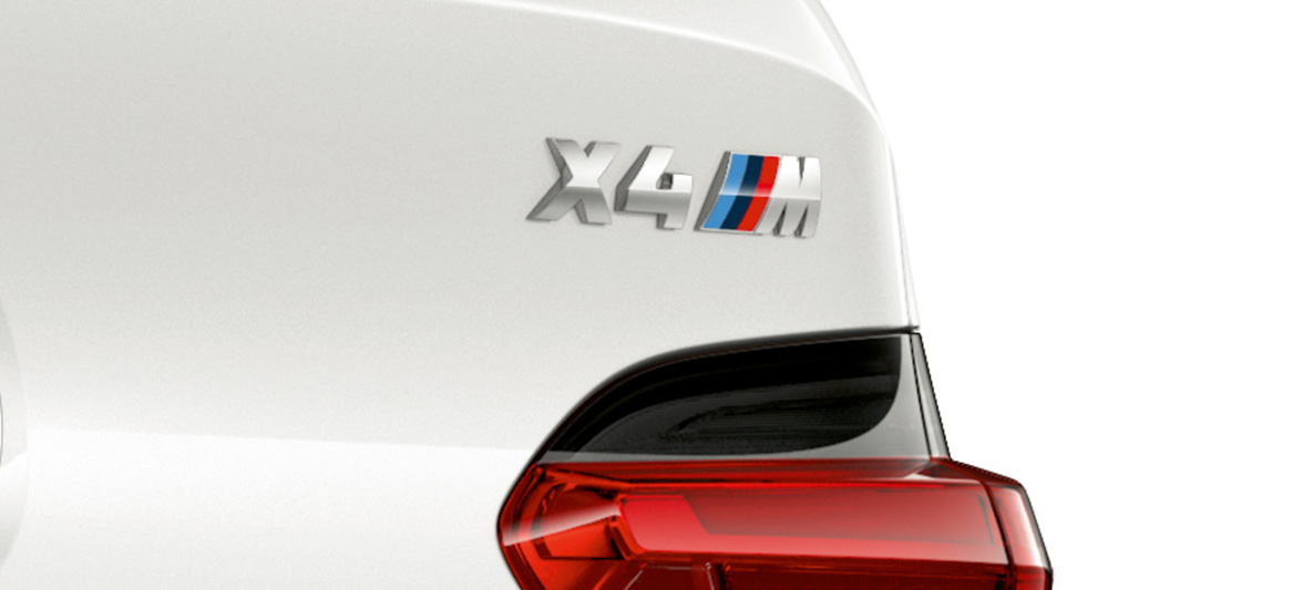 BMW X4 M, insigne du modèle. Extérieur de la BMW X4 M en Alpinweiß, vue en gros plan de l’arrière avec insigne du modèle.