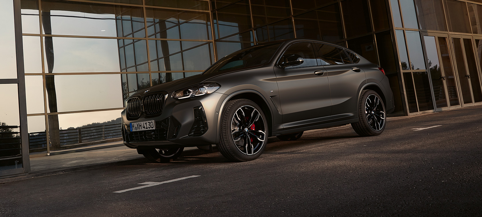 Vue de trois quarts face BMW X4 M40i G02 LCI 2021 Facelift BMW X4 M40i G02 LCI 2021 Facelift vue de trois quarts avant devant une façade en verre