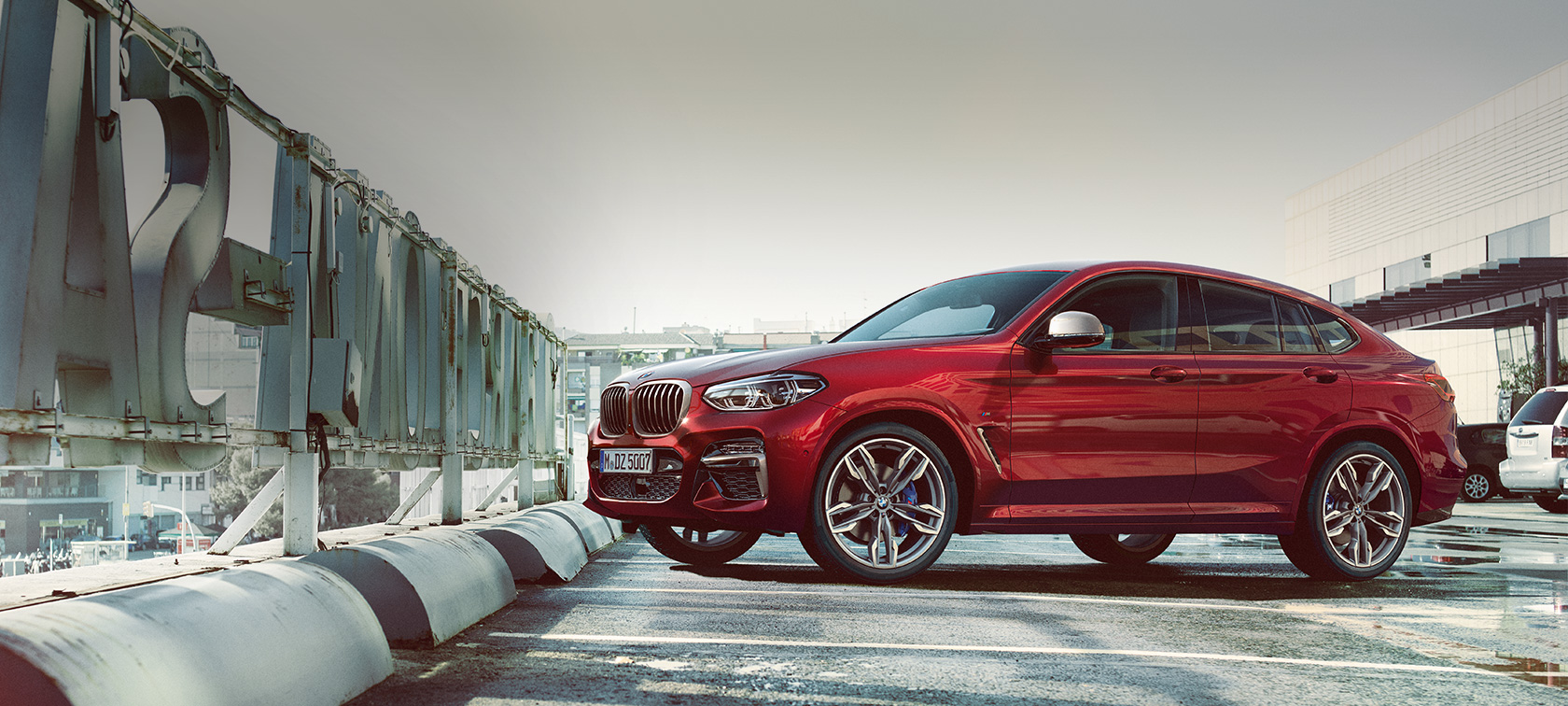 BMW X4 en stationnement, vue de profil BMW X4 M40i G02 2018 en Flamencorot Brillanteffekt vue de profil en stationnement dans un parking à étages
