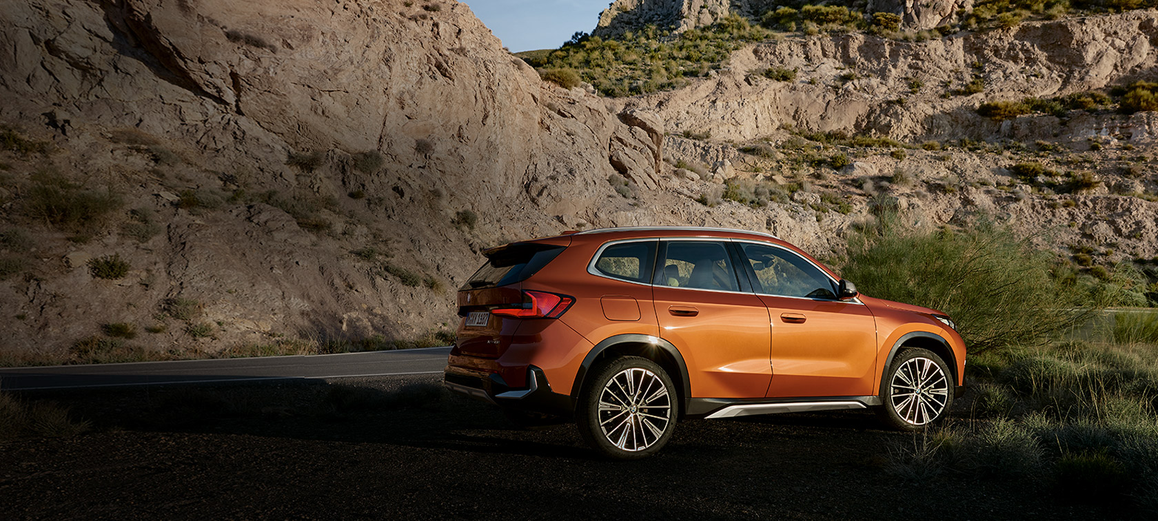 BMW X1 U11 xLine Utah orange metallic, vue de trois quarts avant sur route de campagne