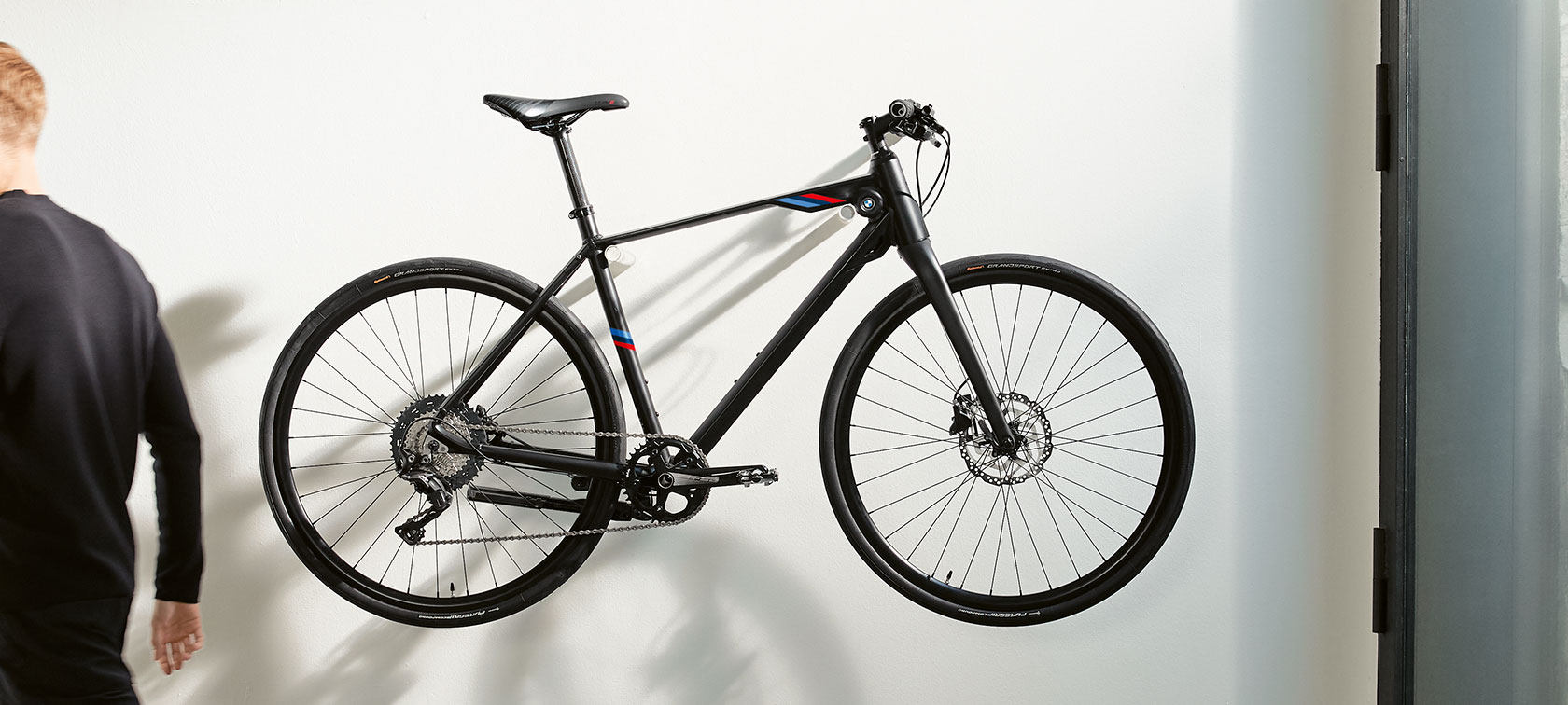 Vélo BMW M Matt Black. La photo montre un vélo BMW M Matt Black avec des bandes BMW M Motorsport suspendu à un support mural.
