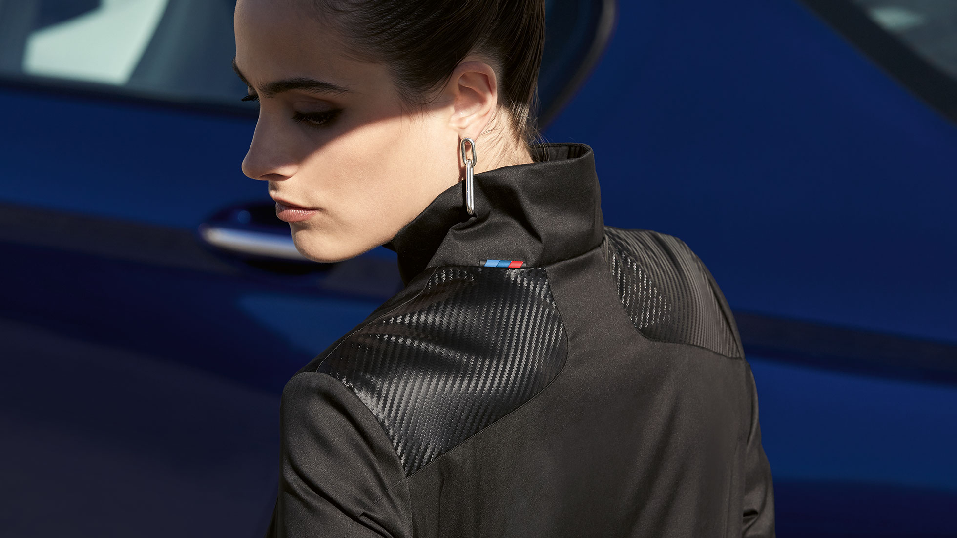 Veste femme BMW M. La femme est présentée portant une veste femme BMW M, de la Collection BMW M. Detail du mélange de matières.