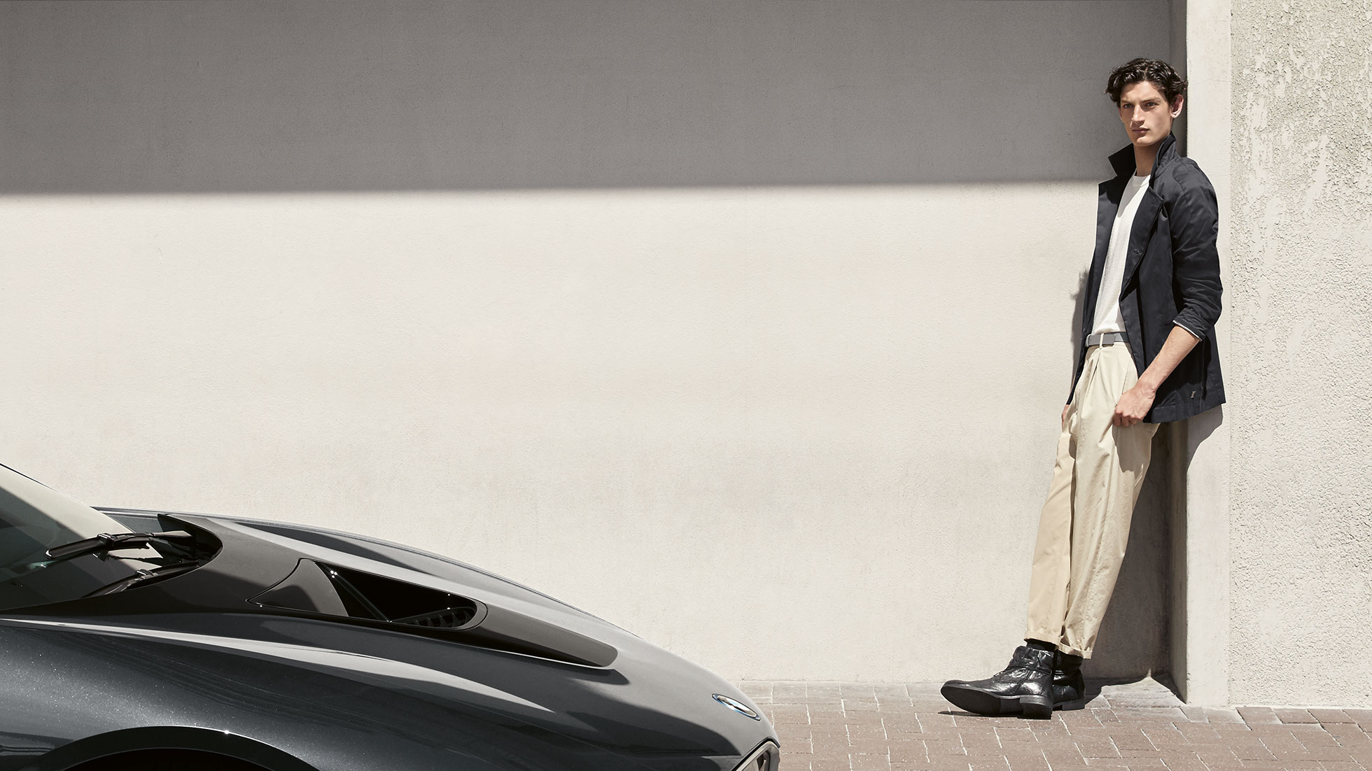 Collection BMW i. La photo montre un homme appuyé contre un mur et portant une veste homme BMW i, de la Collection BMW i.